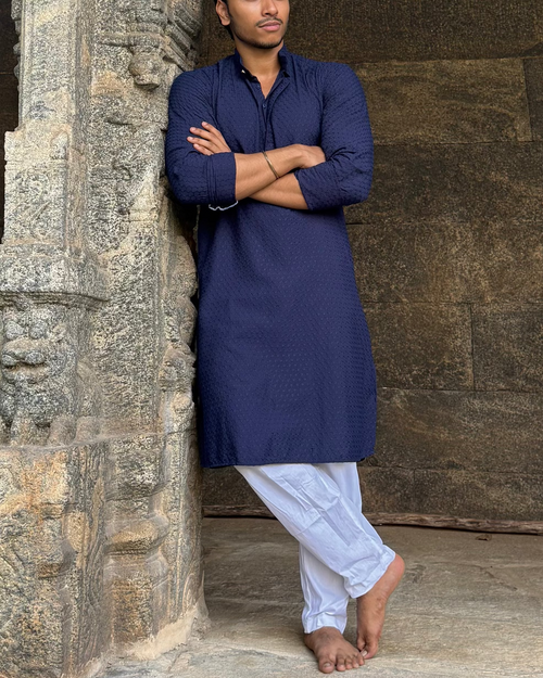 Man in a blue kurta standing in front of an ancient stone wall
