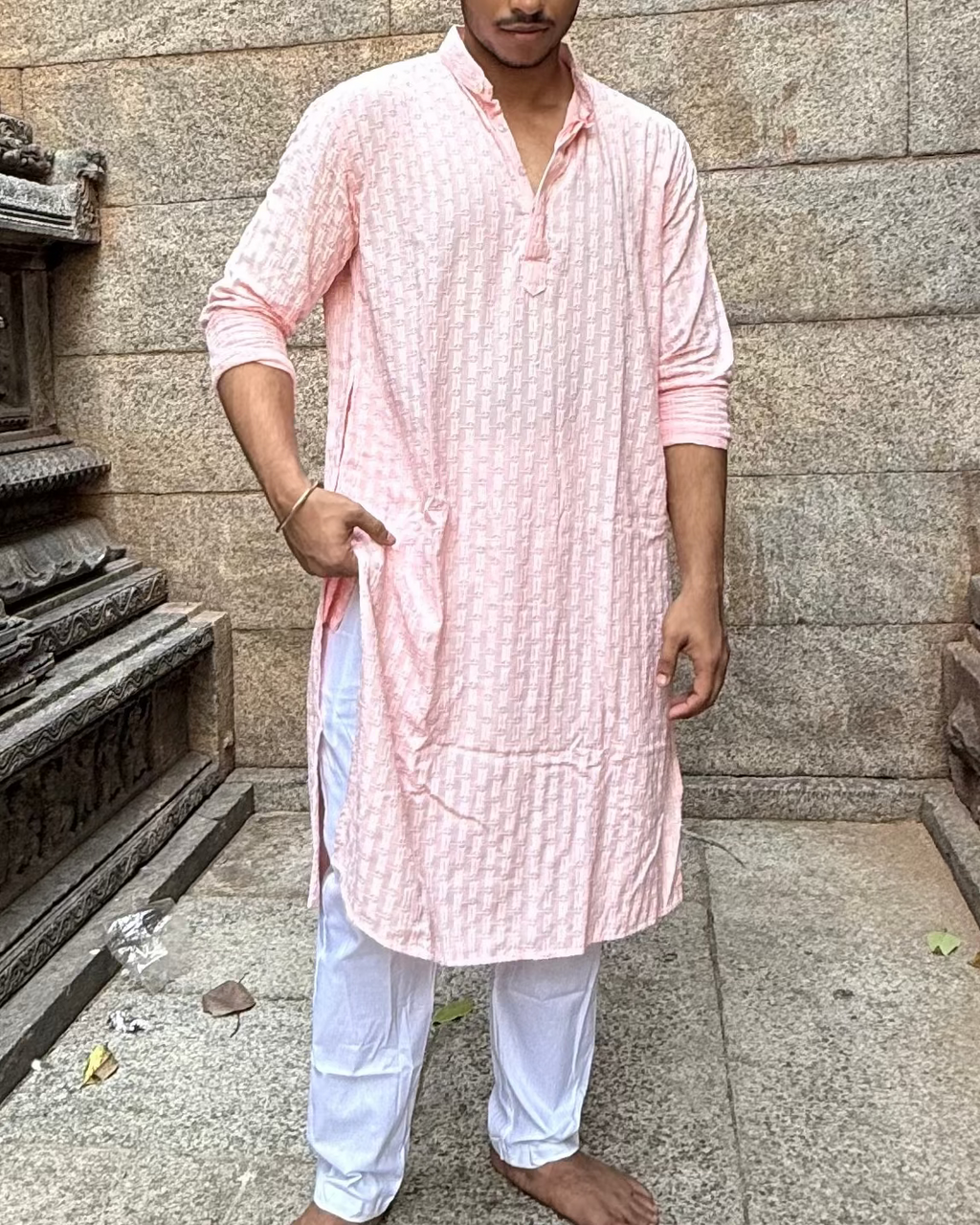 Man in a pink kurta standing in a stone temple corridor