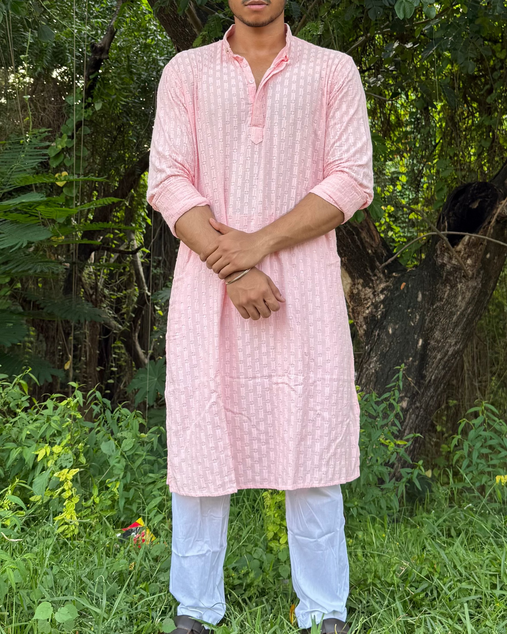 Man wearing a pink kurta standing in a forested area